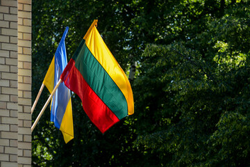 Lithuanian and Ukrainian flags outdoors, green tress in the background