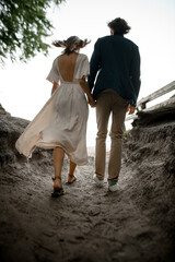 Man and his wife, holding hands, walk along a sandy path