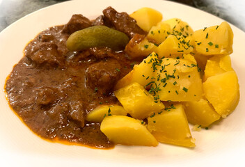 A classic Viennese beef goulash served with salted boiled potatoes and a pickled cucumber on a...