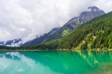 Fototapeta na wymiar Serene Antholzer See Lake Surrounded by Lush Green Mountains under a Cloudy Sky, South Tyrol, Italy
