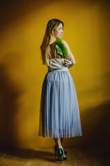Portrait of a blonde girl against a yellow wall. Full-length in a skirt