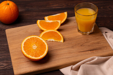 Few slices of orange and a glass of juice on a wooden cutting board.