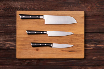 Three kitchen knives laying on a cutting board. Top View.