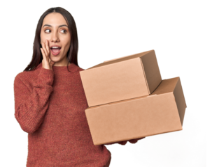 Caucasian young woman with moving boxes on studio background is saying a secret hot braking news and looking aside