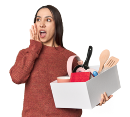 Caucasian young woman holding a box for moving on studio background shouting and holding palm near opened mouth.