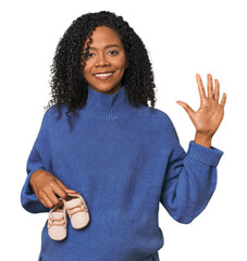 Pregnant woman with baby shoes in studio smiling cheerful showing number five with fingers.