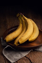 Bunch of bananas on wooden plate, highlighted by soft lighting
