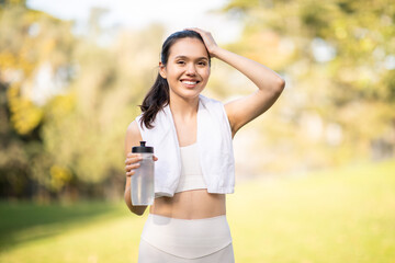 A radiant, smiling woman takes a break from her workout, holding a water bottle