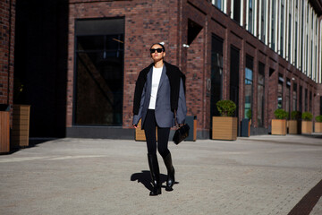 Stylish fashion woman strolls down the street in multilayer clothes oversized blazer, black leggings, and knee high rubber boots. Fashionable outfit, street style
