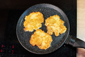 Golden-brown potato pancakes frying in a speckled non-stick pan on a hob.