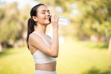 A serene woman in sportswear enjoys a refreshing drink from a water bottle, eyes closed