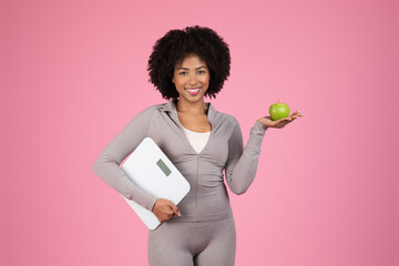 Fit black woman with scales and apple on pink background