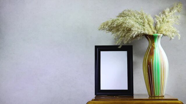 empty picture frame mockup and golden reeds plant vase on wooden table near grunge wall, autumn fall concept