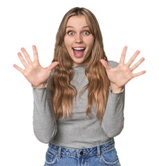 Studio portrait of a blonde Caucasian woman receiving a pleasant surprise, excited and raising...