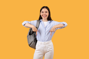 Happy female student with backpack pointing down and smiling