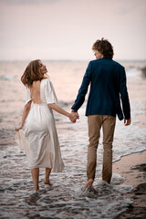 Newlyweds are walking in the water along the seashore, holding hands and looking into each other's eyes