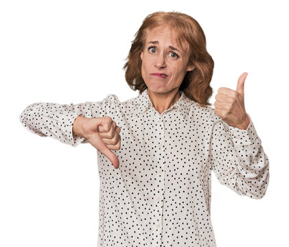 Redhead mid-aged Caucasian woman in studio showing thumbs up and thumbs down, difficult choose concept