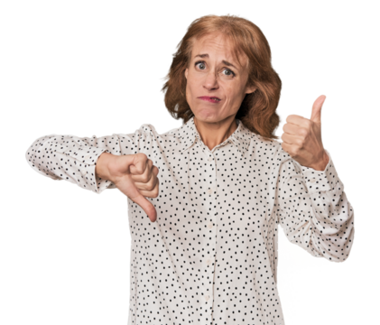 Redhead mid-aged Caucasian woman in studio showing thumbs up and thumbs down, difficult choose concept