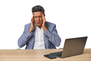 Elegant businessman at desk with laptop touching temples and having headache.