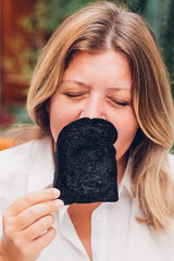 Woman closes her eyes to deeply inhale the aroma of charcoal bread, engaging in a full sensory...