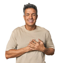 Middle-aged Latino man laughing keeping hands on heart, concept of happiness.