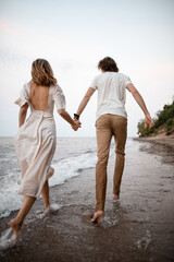 Young couple in wet clothes walk hand in hand on the water by the sea