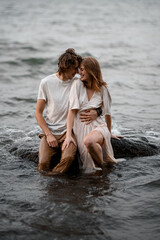 Happy smiling young couple in wet clothes sitting on a rock in the water