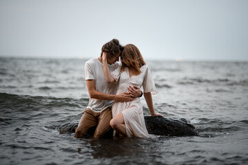 Young couple sits in the water on a rock and hugging