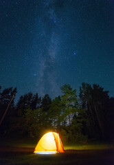 dreamy nighttime scene with a warm yellow tent illuminated by a lantern, and the shimmering Milky Way and stars creating a serene and magical atmosphere in the background. - 755048042