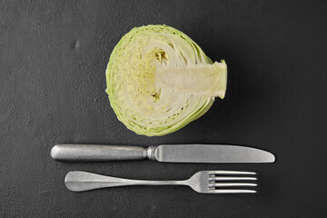 White cabbage in a cut, fork and knife on a black stone tabletop