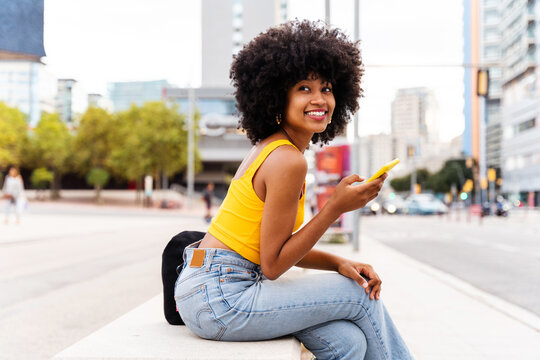 Beautiful young black woman with curly afrp hair style and colorful clothing strolling  outdoors in the city