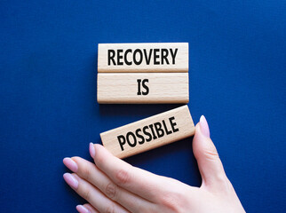 Recovery is possible symbol. Concept words Recovery is possible on wooden blocks. Beautiful deep blue background. Businessman hand. Business and Recovery is possible concept. Copy space.