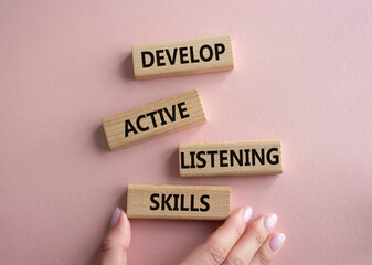Listening skills symbol. Concept word Develop active listening skills on wooden blocks. Beautiful pink background. Businessman hand. Business and Develop active listening skills concept. Copy space