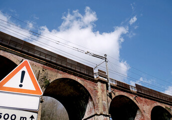 Red solid brick railway bridge, with warning road signs to the left of the structure, next to a road  - 755053010