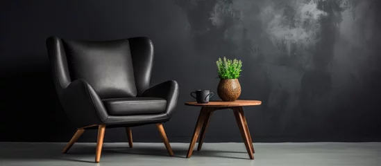 Fotobehang A cosy armchair and a minimalistic coffee table are placed against a black wall. On the table, there is a potted plant, creating a simple and elegant interior design. © Vusal