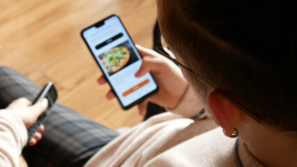 A young man choosing pizza in an online restaurant using a smartphone