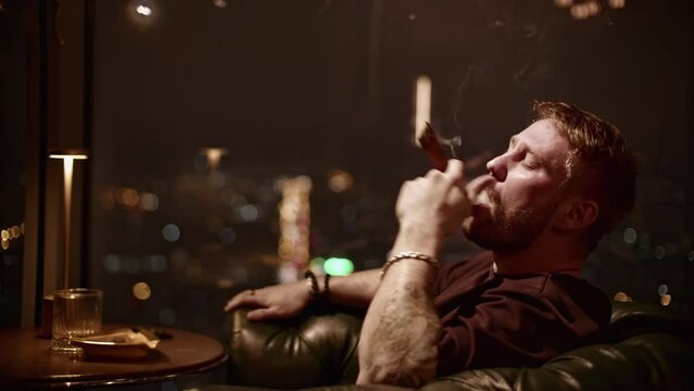 Brutal man smokes cigar. Media. Attractive man with beard smokes cigar coolly. Cinematic cigar smoking with brutal man in restaurant