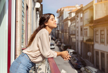 Serene young woman leaning on balcony railing at home