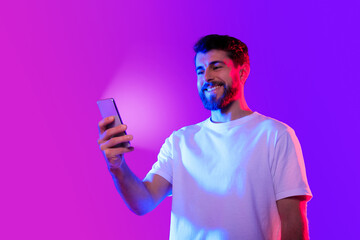 Cheerful caucasian man scrolling through a smartphone app, neon background