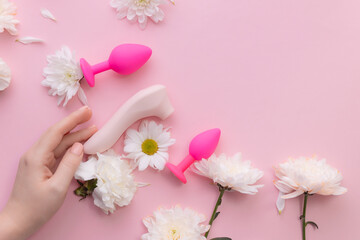 Top view woman hand and vacuum stimulator, set bung on pink background with flowers. Concept erotic...