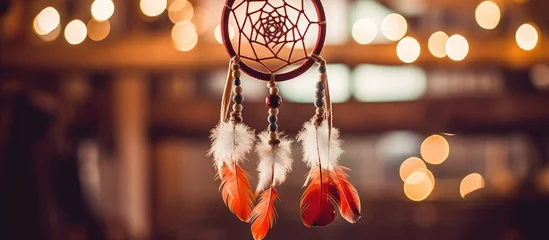Photo sur Plexiglas Style bohème A handmade dream catcher adorned with feathers, threads, and beads is suspended from the ceiling. In the background, soft lights add a warm glow to the scene.