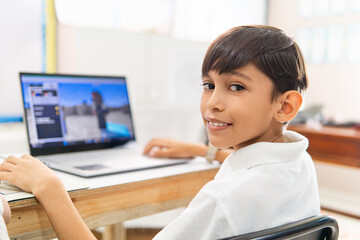 Portrait of Latin american elementary boy using a laptop in class. Technology concept.