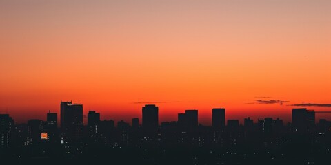 Fototapeta na wymiar Warm sunset hues bathe a cityscape silhouette, with a vivid sun dipping below the horizon amidst skyscrapers.
