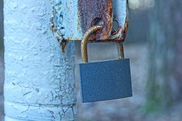 one closed iron rusty  industrial modern gray padlock hanging on a rusty bracket during the day on...