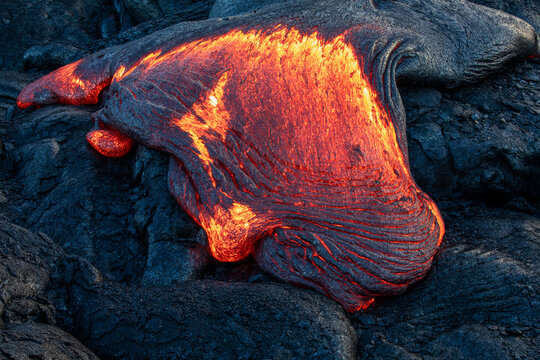 Detail of glowing flowing red hot lava with black ripples of hardened black lava around