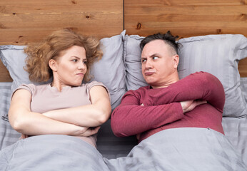 Man and a woman are lying in bed under a gray blanket, and they look at each other with...
