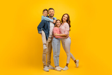 Family Portrait. Happy Young Parents And Their Kids Embracing Over Yellow Background