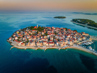 Primosten, Croatia - Aerial view of Primosten peninsula, St. George's Church and old town on a sunny summer morning in Dalmatia, Croatia. Golden sky, yacht marina at sunrise on the Adriatic sea coast