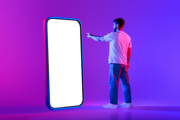 Young man points to big cellphone screen against neon backdrop