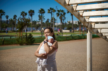 Woman carrying her newborn baby while walking together on the city on warm sunny day